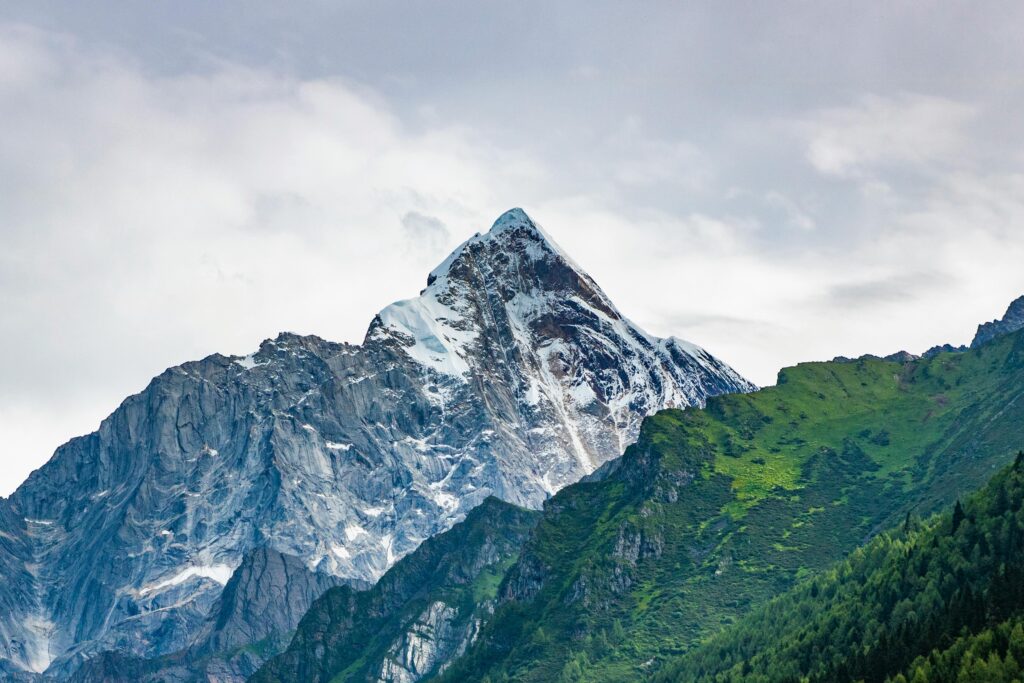 Stunning view of a snow-capped mountain peak surrounded by green slopes and cloudy skies.